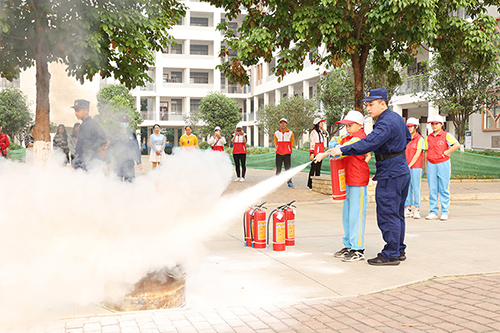 县消防救援大队队员指导学生正确使用干粉灭火器。